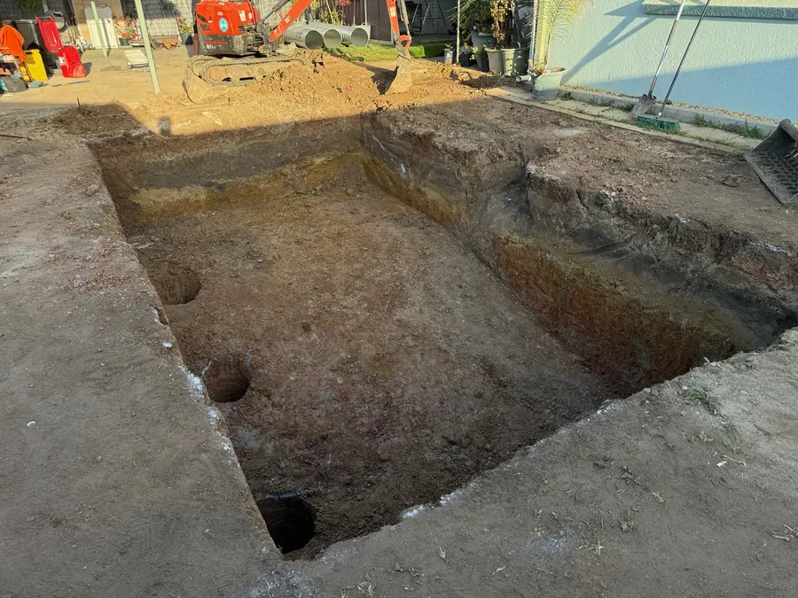 After: the pool dug out in the same backyard, with clean straight walls and pier holes in the floor
