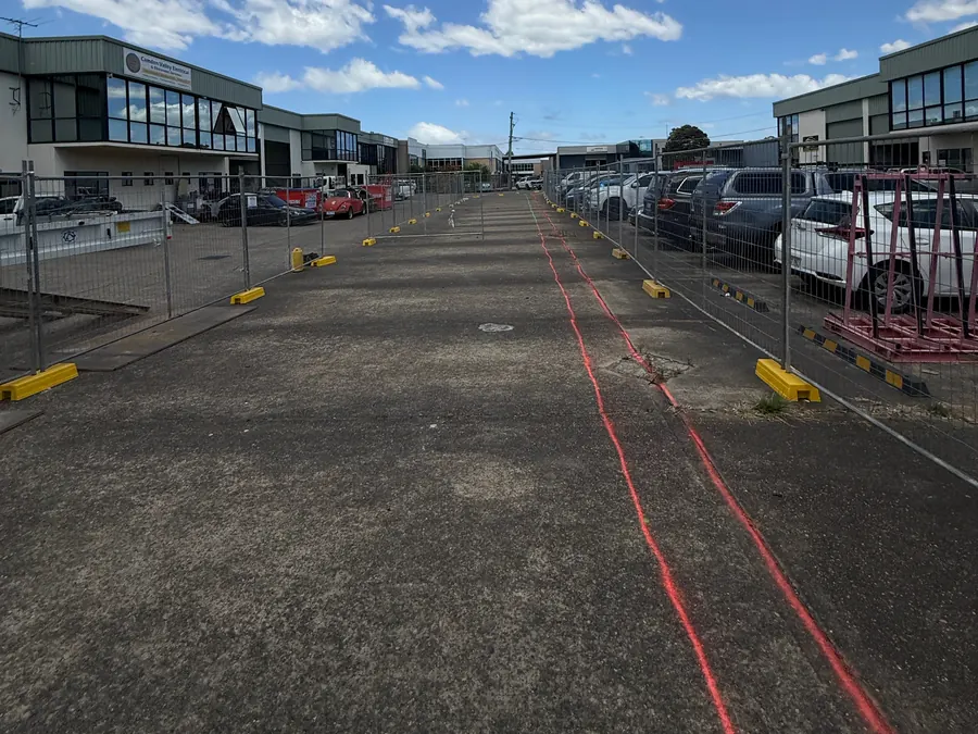 Before: trench line marked out in red paint along a fenced concrete lane in an industrial estate